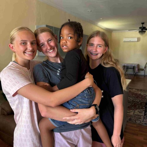 Three female volunteers from the Immanuel CRC youth group embrace a young Bahamian child, showcasing the relational ministry and life development programs prioritized during Many Hands impact trips.