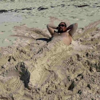 An impact trip participant finds rest and joy in God's creation while buried up to his shoulders in white sand during a team beach fellowship afternoon.