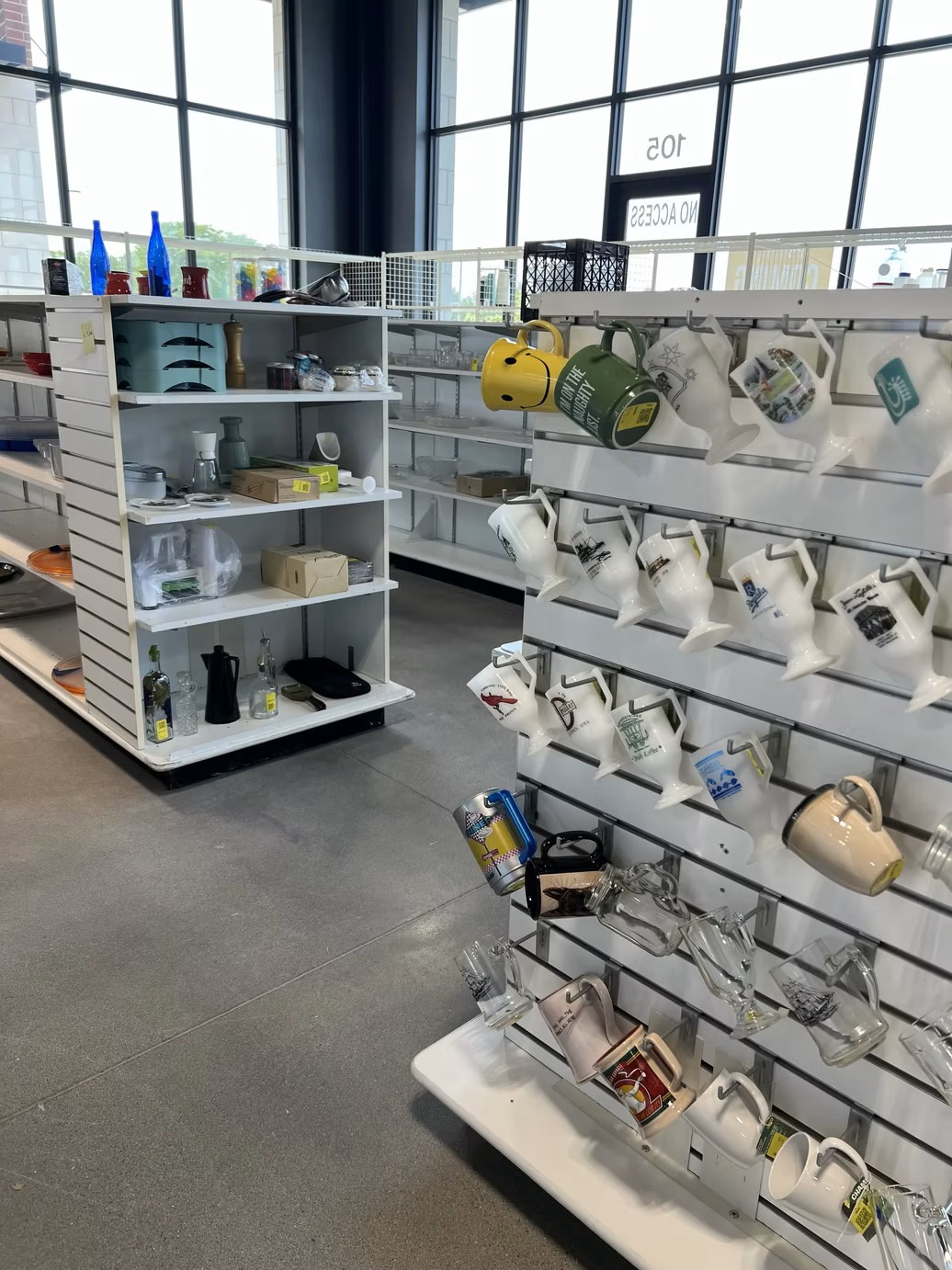 Display shelves filled with coffee mugs, glassware, and kitchen housewares at the new Jordan Creek Thrift Store.