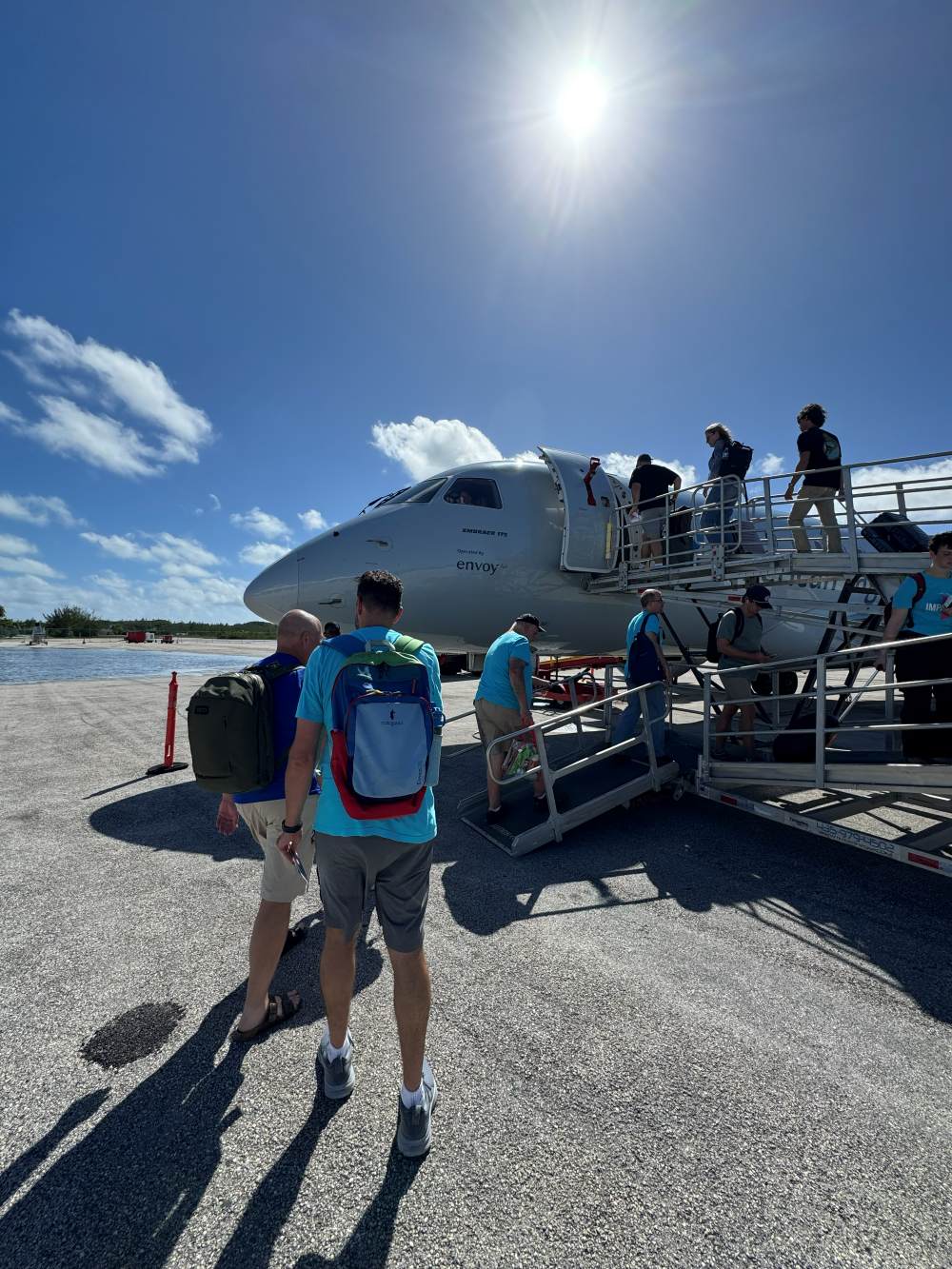Many Hands team members climb the airstrip stairs under a clear sunny sky to board their flight home after a transformative impact week in Abaco.