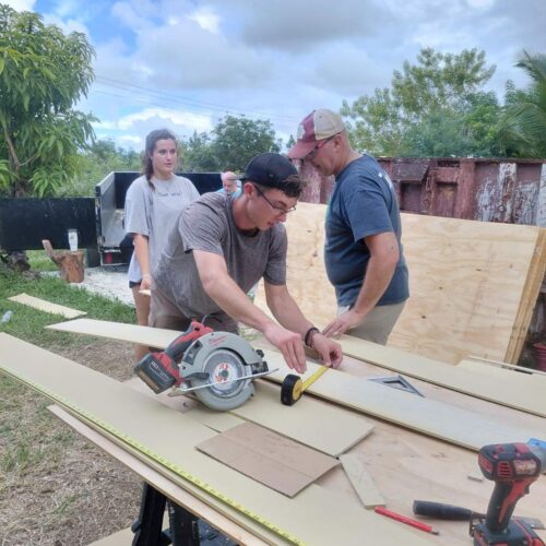 A volunteer uses a circular saw to trim siding boards during a home rebuild project.