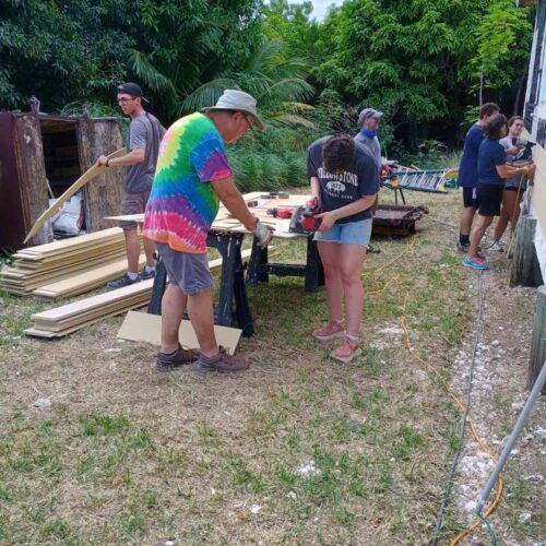 Impact team members coordinate lumber cutting and siding prep in the yard to accelerate home reconstruction efforts for local Bahamian families.