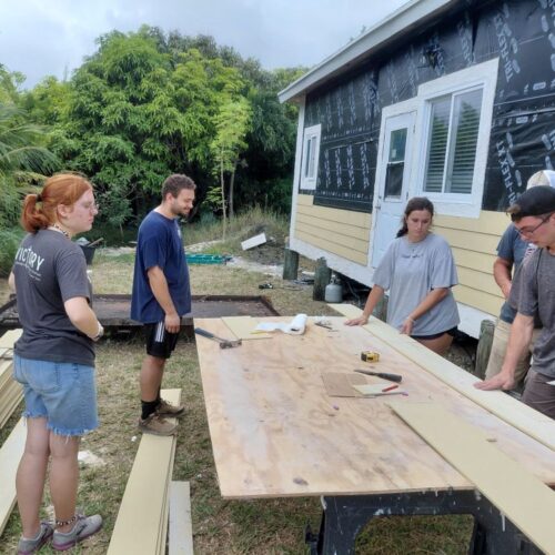 Volunteers gather around the outdoor cutting station to review siding measurements for Wain's home restoration in Abaco.