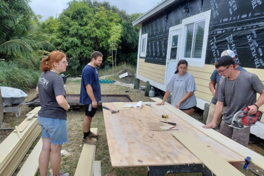 Volunteers gather around the outdoor cutting station to review siding measurements for Wain's home restoration in Abaco.