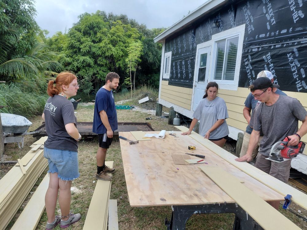 Volunteers gather around the outdoor cutting station to review siding measurements for Wain's home restoration in Abaco.