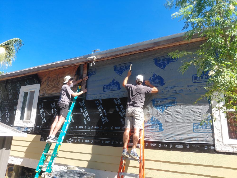 Impact team volunteers work on extension ladders to install weather-resistant house wrap on a home structure in Abaco.