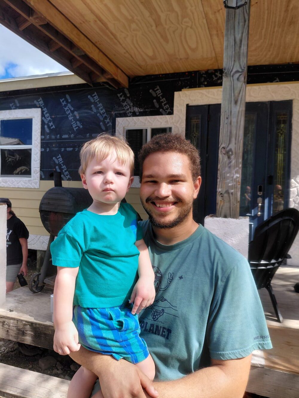 A Many Hands impact team volunteer smiles while holding a young child.