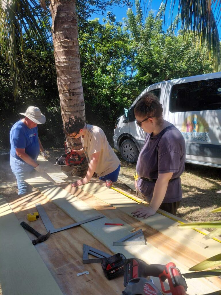 Volunteers operate a circular saw at an outdoor work station to cut siding boards for a hurricane recovery rebuild in Abaco.
