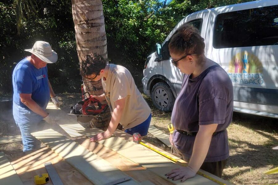 Volunteers operate a circular saw at an outdoor work station to cut siding boards for a hurricane recovery rebuild in Abaco.