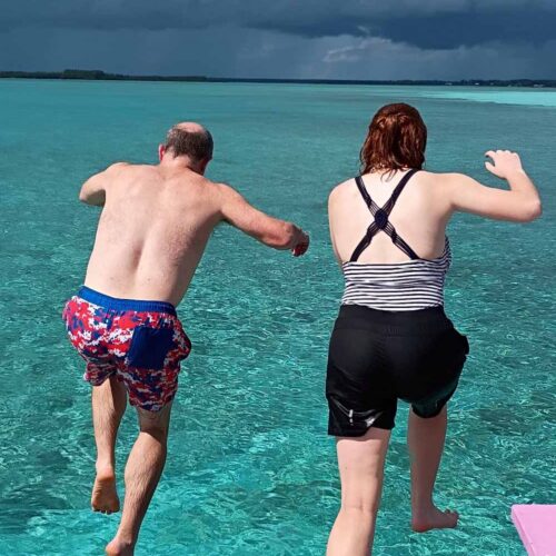 Many Hands impact trip participants leap off a wooden dock into crystal-clear turquoise waters during a team rest and fellowship day in Abaco.