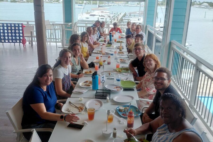 Impact trip team members gather along a long table for a shared fellowship meal overlooking the water in Abaco.