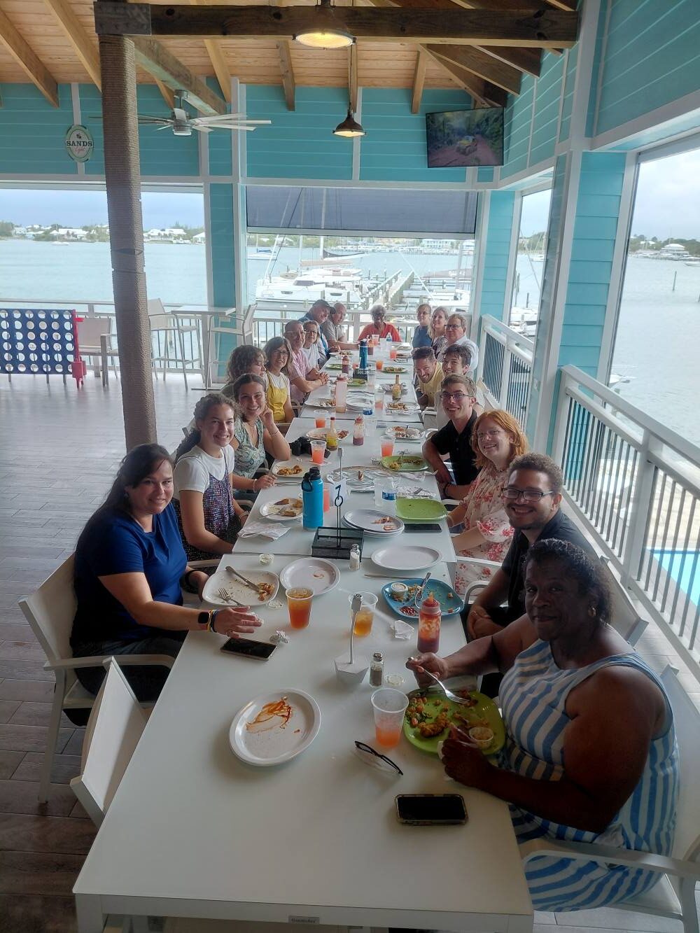Impact trip team members gather along a long table for a shared fellowship meal overlooking the water in Abaco.