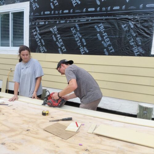 Impact team volunteers work together to measure and prepare exterior siding materials for a home restoration project in Abaco.