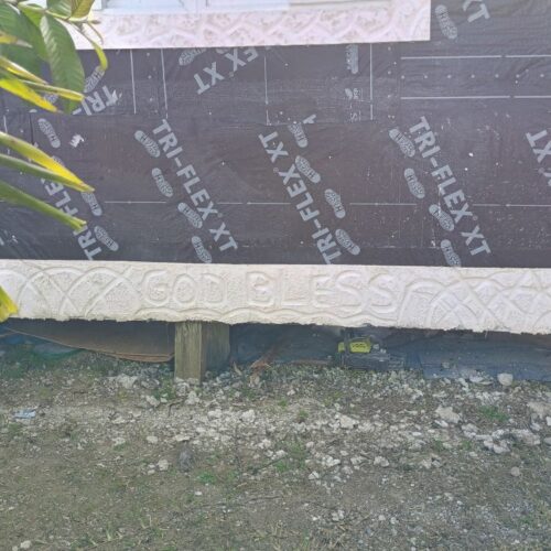 The concrete foundation of a rebuilt home in Abaco inscribed with the words 'God Bless,' reflecting faith and hope amidst hurricane recovery.